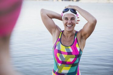 Porträt einer lachenden, lächelnden Freiwasserschwimmerin, die ihre Badekappe im Meer anpasst - CAIF05241