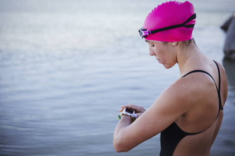 Schwimmerin im Freiwasser, die ihre Smartwatch im Meer überprüft, lizenzfreies Stockfoto