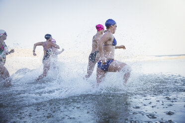 Female open water swimmers running and splashing in ocean surf - CAIF05245