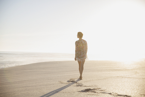 Nachdenkliche, ruhige Frau, die an einem sonnigen Sommerstrand spazieren geht, lizenzfreies Stockfoto