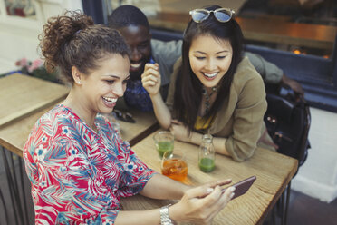 Young women friends using smart phone at sidewalk cafe - CAIF05254