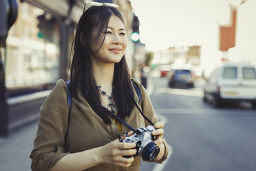 Lächelnde junge Touristin beim Fotografieren mit der Kamera auf einer städtischen Straße - CAIF05256