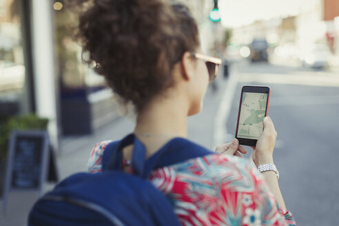 Junge Touristin mit Rucksack, die auf einer städtischen Straße GPS auf ihrem Smartphone benutzt - CAIF05257