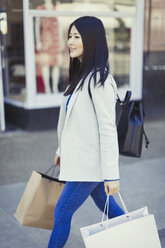 Junge Frau geht mit Einkaufstüten an einem Schaufenster entlang - CAIF05280