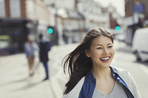 Lächelnde, begeisterte junge Frau, die auf einer sonnigen städtischen Straße spazieren geht, lizenzfreies Stockfoto