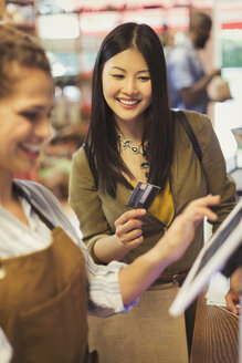 Eine weibliche Kassiererin hilft einem lächelnden Kunden mit einer Kreditkarte an der Kasse eines Lebensmittelladens - CAIF05287