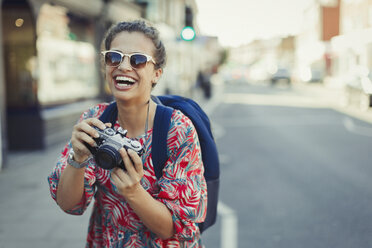 Porträt lachende, begeisterte junge Touristin mit Sonnenbrille beim Fotografieren mit Kamera auf städtischer Straße - CAIF05289