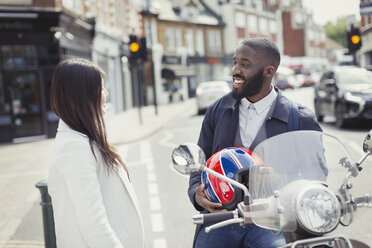 Lächelnder junger Geschäftsmann auf einem Motorroller im Gespräch mit einem Freund auf einer städtischen Straße - CAIF05292