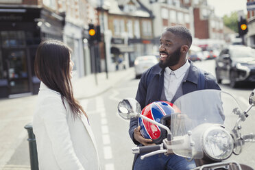 Smiling young businessman on motor scooter talking to friend on urban street - CAIF05292