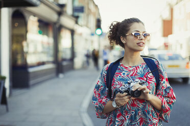Junge Touristin mit Sonnenbrille und Kamera auf einer Straße - CAIF05297