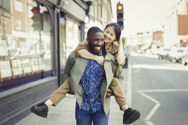 Playful young couple piggybacking on urban street - CAIF05303