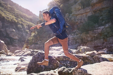Junger Mann mit Rucksack beim Wandern und Springen über Felsen - CAIF05307
