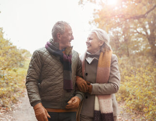 Zärtliches älteres Paar, das Arm in Arm auf einem Weg im Herbstpark spazieren geht - CAIF05313