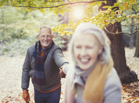 Verspieltes älteres Paar hält Hände im Herbstpark, lizenzfreies Stockfoto