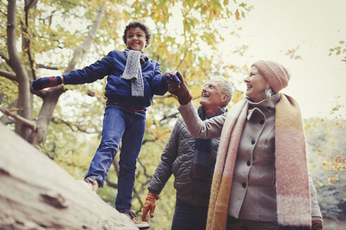 Großeltern gehen mit ihrem Enkel auf einem Baumstamm im Herbstpark spazieren - CAIF05317