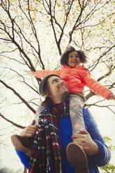 Vater trägt begeisterte Tochter auf den Schultern unter einem Herbstbaum im Park - CAIF05320