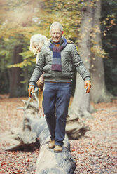 Älteres Paar geht auf einem Baumstamm im Herbstwald spazieren - CAIF05324