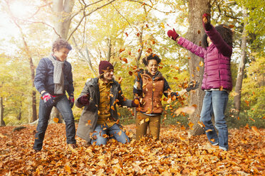 Playful young family throwing leaves in autumn woods - CAIF05325