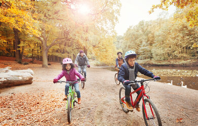 Young family bike riding along pond in autumn park - CAIF05328