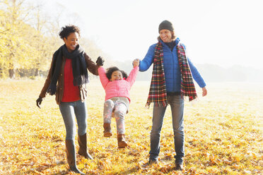 Parents swinging daughter in sunny autumn park grass - CAIF05333