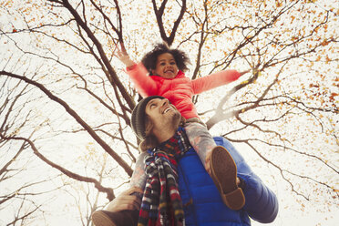 Father carrying daughter on shoulders under tree in autumn park - CAIF05340