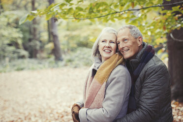 Lächelndes älteres Paar, das sich im Herbst im Park umarmt - CAIF05347