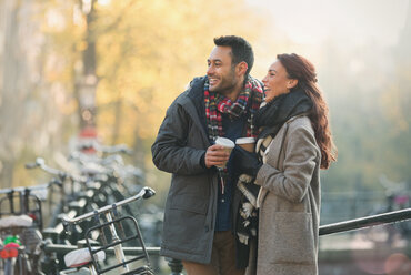 Lächelndes junges Paar in warmer Kleidung trinkt Kaffee in der Stadt - CAIF05350