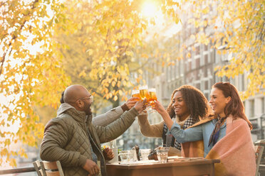 Smiling friends toasting beer glasses at autumn sidewalk cafe - CAIF05351