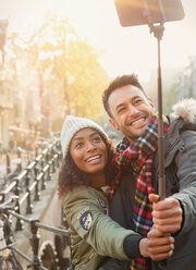 Lächelndes junges Paar nimmt Selfie mit Selfie-Stick auf städtischen Straße - CAIF05352