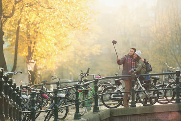 Junges Paar mit Fahrrädern macht Selfie mit Selfie-Stick auf der Herbstbrücke, Amsterdam - CAIF05353