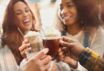 Lächelnde Freunde stoßen in einem Café mit Milchshakes und Kaffeetassen an - CAIF05356