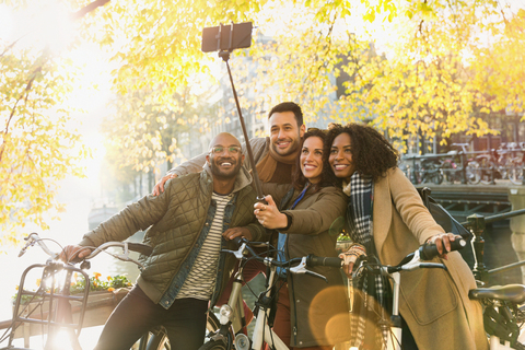 Smiling friends with bicycle taking selfie with selfie stick on urban bridge stock photo
