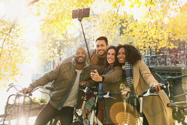 Smiling friends with bicycle taking selfie with selfie stick on urban bridge - CAIF05357