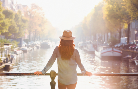 Frau mit Hut und Blick auf eine sonnige Grachtenlandschaft im Herbst, Amsterdam, lizenzfreies Stockfoto