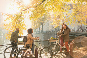 Friends with bicycles along sunny autumn canal in Amsterdam - CAIF05361