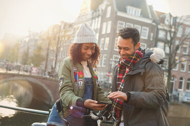 Junges Paar mit Fahrrad und Handy auf einer Brücke, Amsterdam - CAIF05364