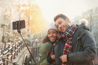 Affectionate couple hugging and taking selfie with selfie stick on autumn bridge, Amsterdam - CAIF05381