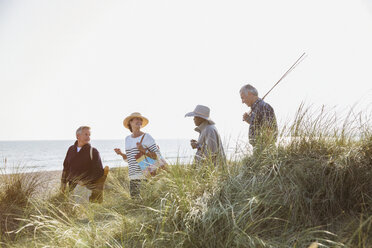 Senior couples with fishing pole walking in sunny beach grass - CAIF05385