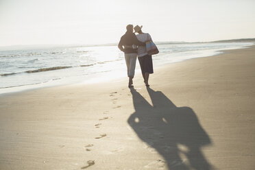Zärtliches reifes Paar, das sich umarmt und am sonnigen Strand spazieren geht - CAIF05390