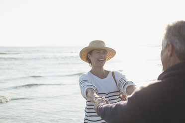 Playful mature couple holding hands on sunny ocean beach - CAIF05394