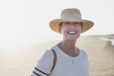Portrait lächelnde reife Frau mit Strohhut am sonnigen Sommerstrand - CAIF05401