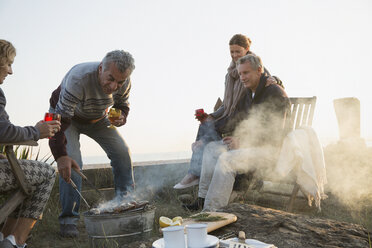 Ältere Paare beim Grillen und Weintrinken am Strand bei Sonnenuntergang - CAIF05405