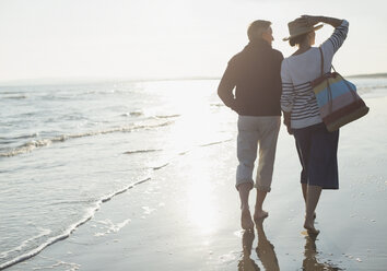 Älteres Paar spaziert am sonnigen Strand - CAIF05407