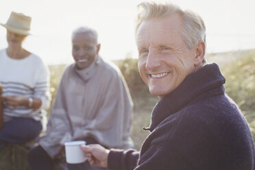 Portrait lächelnder älterer Mann trinkt Kaffee mit Freunden am sonnigen Strand - CAIF05408