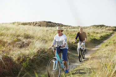 Mature couple riding bicycles on sunny beach grass path - CAIF05417