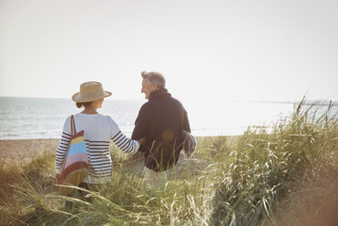 Älteres Paar geht Arm in Arm am sonnigen Strand spazieren - CAIF05419