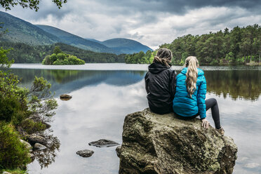 Paar sitzt auf einem Felsen und schaut auf einen ruhigen See, Loch an Eilein, Schottland - CAIF05425