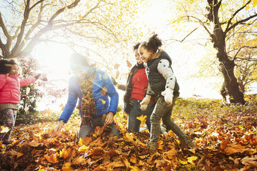 Verspielte junge Familie spielt im Herbst Blätter in sonnigen Park - CAIF05427