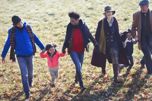 Mehrgenerationenfamilie, die sich an den Händen hält und im sonnigen Herbstpark spazieren geht - CAIF05432