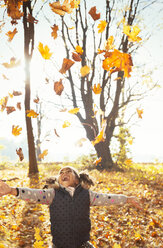 Playful girl throwing leaves overhead in sunny autumn park - CAIF05434